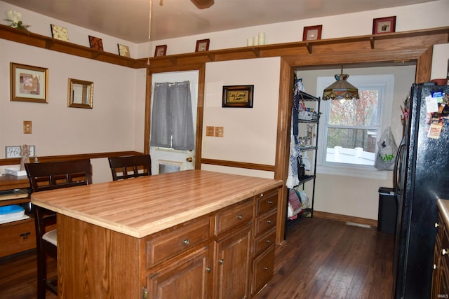 kitchen with black refrigerator, a kitchen bar, pendant lighting, a center island, and dark hardwood / wood-style floors