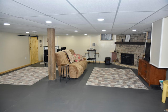 living room with a barn door, a drop ceiling, and a stone fireplace