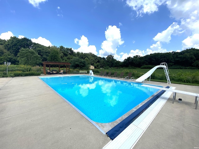 view of swimming pool featuring a patio, a pergola, a diving board, and a water slide