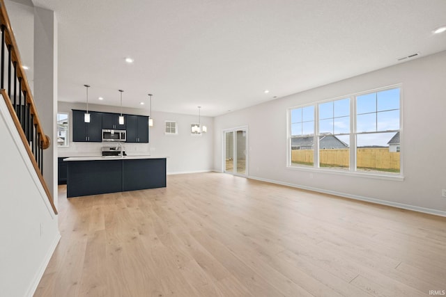 unfurnished living room featuring a notable chandelier and light wood-type flooring