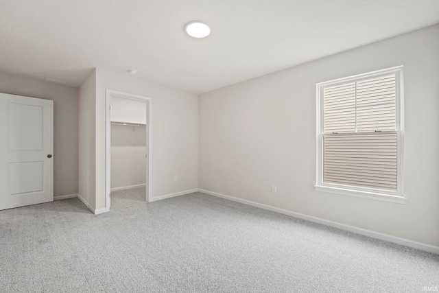 unfurnished bedroom featuring a closet, a walk in closet, and light carpet