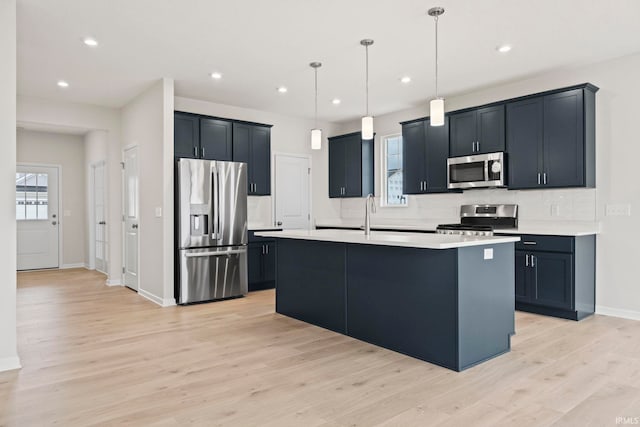 kitchen with decorative light fixtures, tasteful backsplash, a center island with sink, light hardwood / wood-style flooring, and appliances with stainless steel finishes