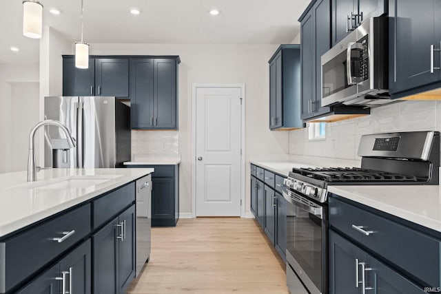 kitchen featuring hanging light fixtures, backsplash, appliances with stainless steel finishes, sink, and light hardwood / wood-style flooring