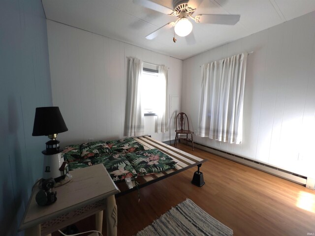 bedroom with ceiling fan, light wood-type flooring, and a baseboard heating unit