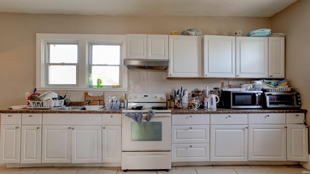 kitchen featuring dark stone counters, white range, light tile floors, sink, and white cabinetry