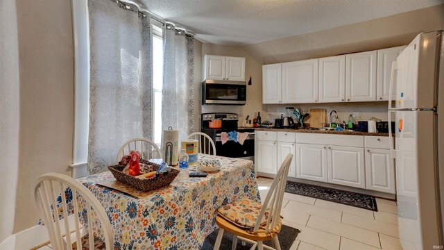 kitchen with lofted ceiling, stainless steel appliances, light tile floors, sink, and white cabinets