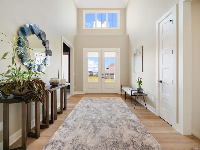 entrance foyer featuring light hardwood / wood-style floors, french doors, a wealth of natural light, and a towering ceiling