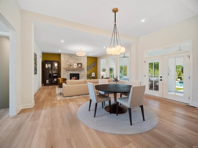 dining room with brick wall, light hardwood / wood-style flooring, french doors, and a fireplace