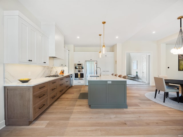 kitchen with white cabinetry, light hardwood / wood-style floors, tasteful backsplash, a kitchen island with sink, and pendant lighting