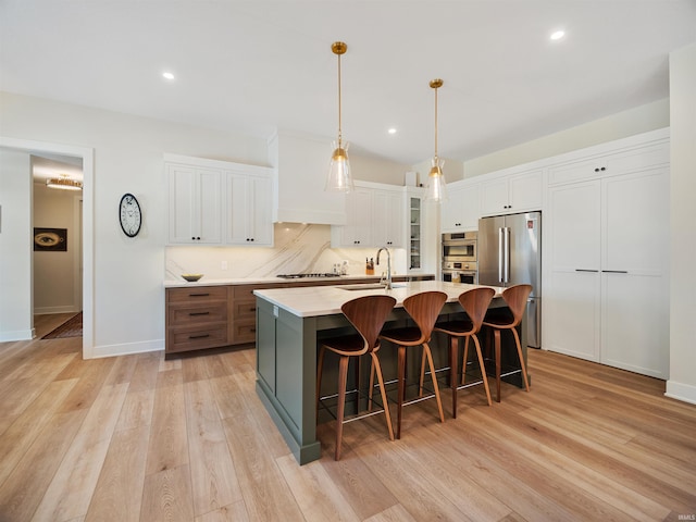 kitchen with white cabinets, sink, tasteful backsplash, light wood-type flooring, and an island with sink