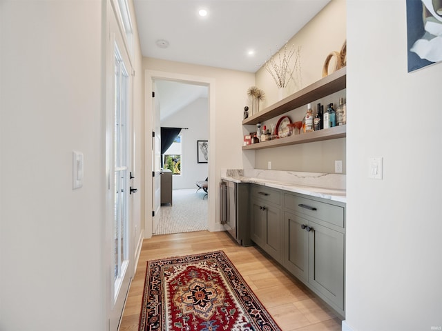 bar with light hardwood / wood-style floors, gray cabinetry, and light stone countertops