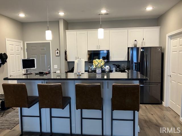 kitchen featuring decorative light fixtures, white cabinets, light hardwood / wood-style flooring, and a kitchen island with sink