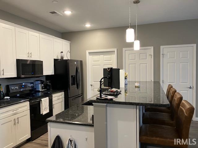 kitchen with decorative light fixtures, white cabinets, stainless steel appliances, light hardwood / wood-style flooring, and a kitchen island with sink