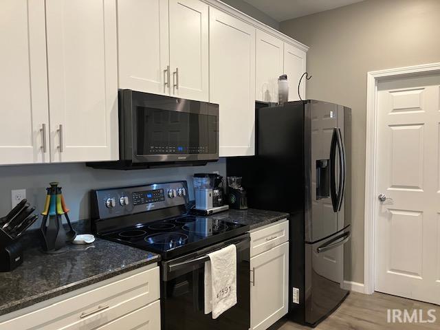 kitchen featuring appliances with stainless steel finishes, dark stone counters, white cabinetry, and light hardwood / wood-style floors