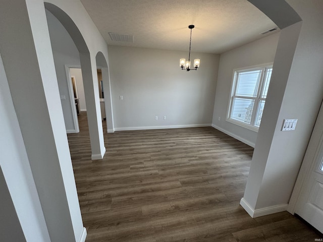 unfurnished dining area featuring dark hardwood / wood-style floors, a textured ceiling, and an inviting chandelier