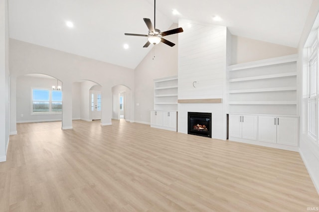 unfurnished living room with high vaulted ceiling, ceiling fan, built in shelves, light hardwood / wood-style floors, and a large fireplace