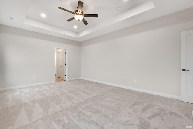 spare room featuring a raised ceiling, ceiling fan, and light carpet