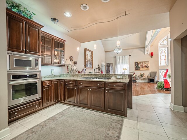 kitchen with a wealth of natural light, kitchen peninsula, appliances with stainless steel finishes, and light stone counters