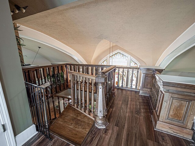 stairway with a textured ceiling, vaulted ceiling, and dark wood-type flooring