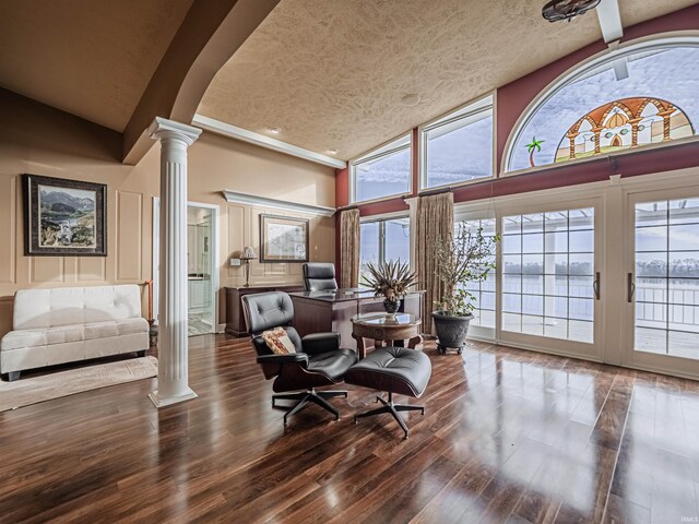 interior space featuring dark hardwood / wood-style floors, high vaulted ceiling, a textured ceiling, and decorative columns