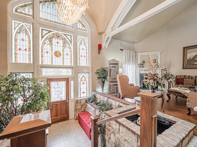 tiled entrance foyer with a chandelier, high vaulted ceiling, and a fireplace