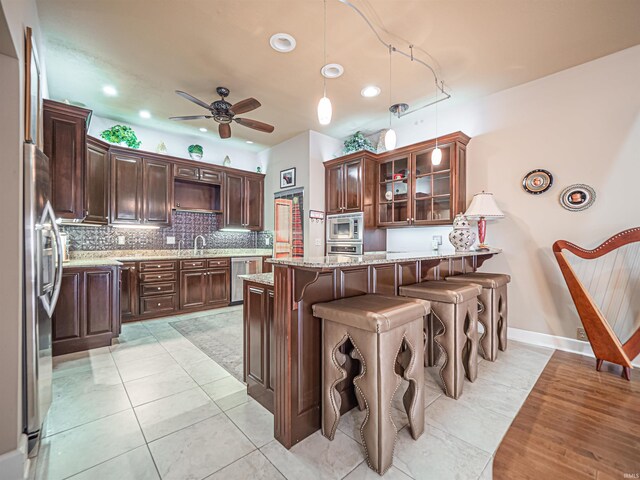 kitchen with ceiling fan, a kitchen bar, stainless steel appliances, pendant lighting, and light stone countertops