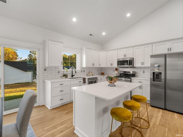 kitchen featuring appliances with stainless steel finishes, a center island, high vaulted ceiling, white cabinets, and sink