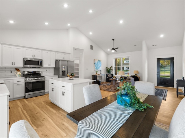 kitchen with ceiling fan, stainless steel appliances, decorative backsplash, a kitchen island, and white cabinets