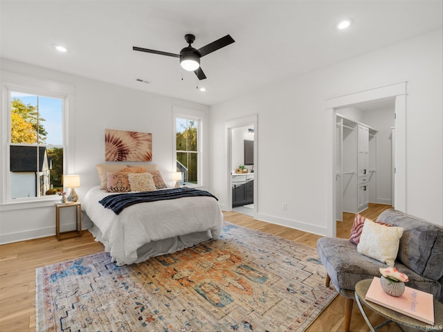 bedroom with ceiling fan, light hardwood / wood-style floors, a walk in closet, and ensuite bath