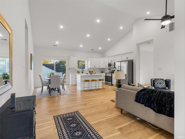 living room featuring ceiling fan, light hardwood / wood-style flooring, and high vaulted ceiling