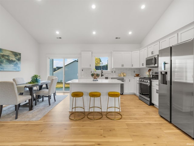 kitchen with lofted ceiling, a kitchen island, appliances with stainless steel finishes, a kitchen breakfast bar, and white cabinets