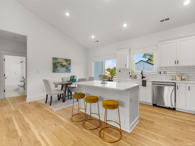 kitchen with a center island, lofted ceiling, white cabinetry, backsplash, and stainless steel dishwasher