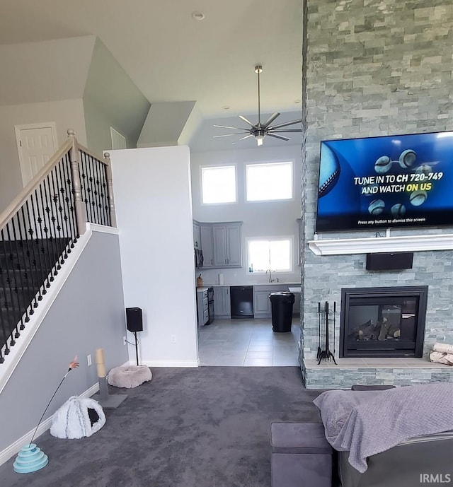 living room with a towering ceiling, ceiling fan, sink, light tile patterned floors, and a stone fireplace