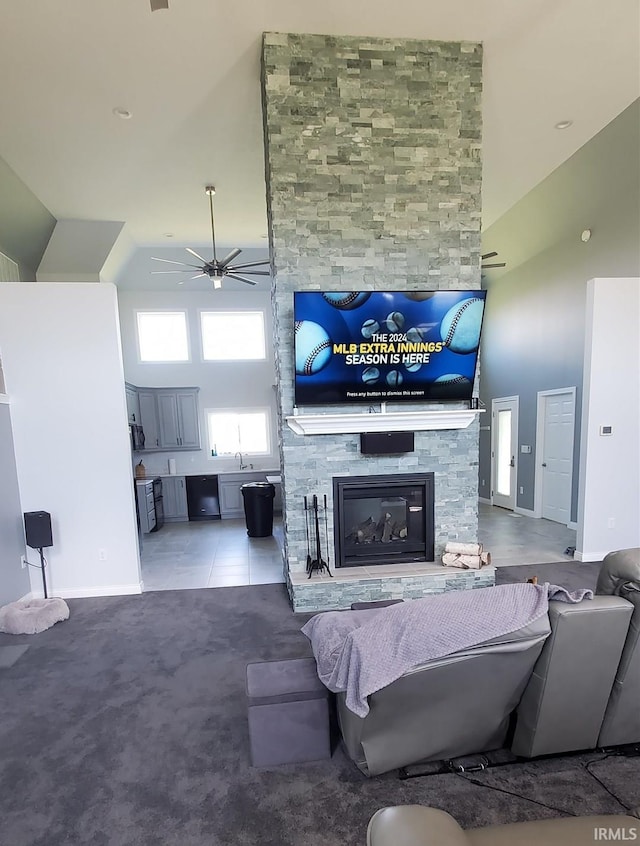 tiled living room with ceiling fan, a stone fireplace, a towering ceiling, and sink