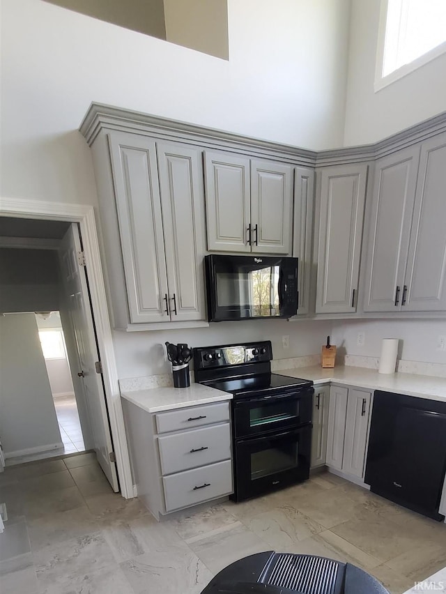 kitchen featuring gray cabinets, a towering ceiling, and black appliances