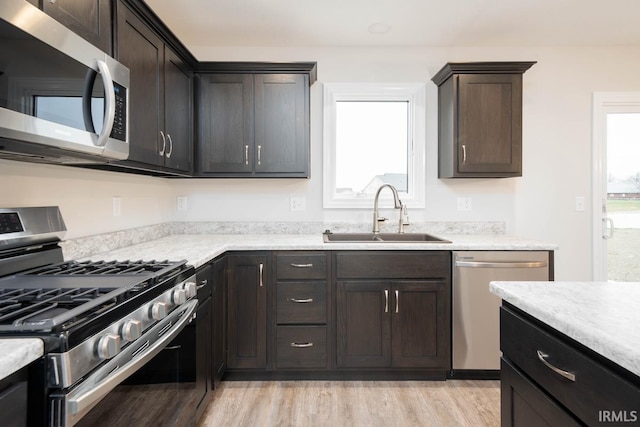 kitchen with appliances with stainless steel finishes, sink, dark brown cabinetry, and light hardwood / wood-style flooring