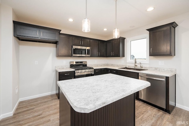 kitchen featuring a kitchen island, decorative light fixtures, sink, stainless steel appliances, and light hardwood / wood-style flooring