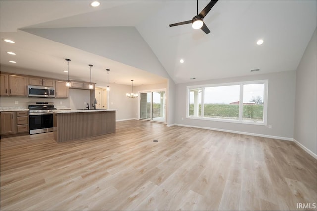 kitchen with appliances with stainless steel finishes, ceiling fan with notable chandelier, pendant lighting, light hardwood / wood-style floors, and a center island with sink