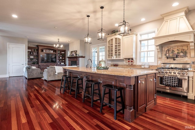 kitchen featuring a breakfast bar area, double oven range, dark wood-type flooring, an island with sink, and light stone counters