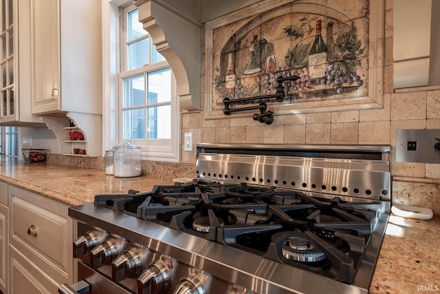 kitchen with backsplash, stainless steel range with gas stovetop, white cabinetry, and light stone counters