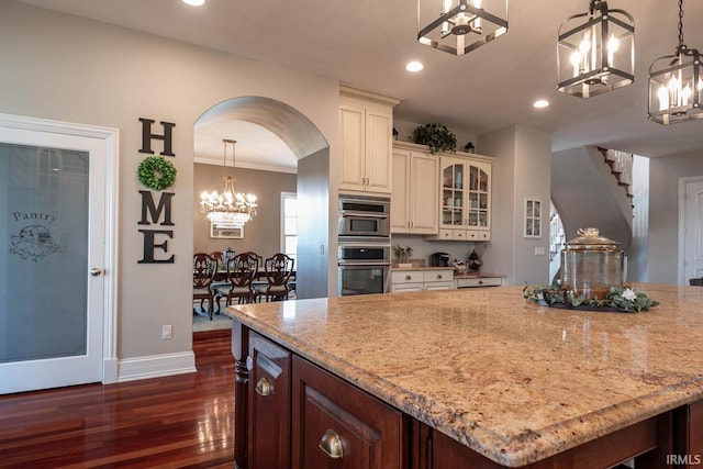 kitchen with a center island, hanging light fixtures, dark hardwood / wood-style flooring, light stone counters, and cream cabinetry