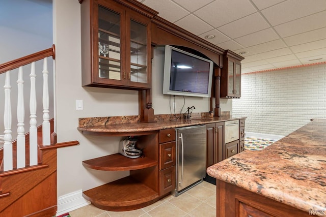 bar featuring a paneled ceiling, light tile floors, sink, refrigerator, and stone counters