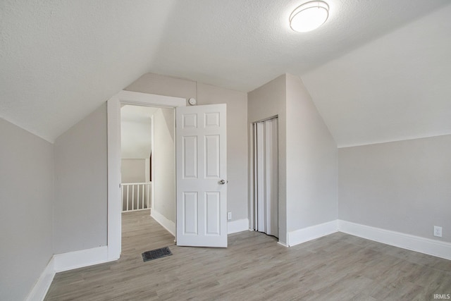 additional living space featuring light hardwood / wood-style flooring, a textured ceiling, and lofted ceiling