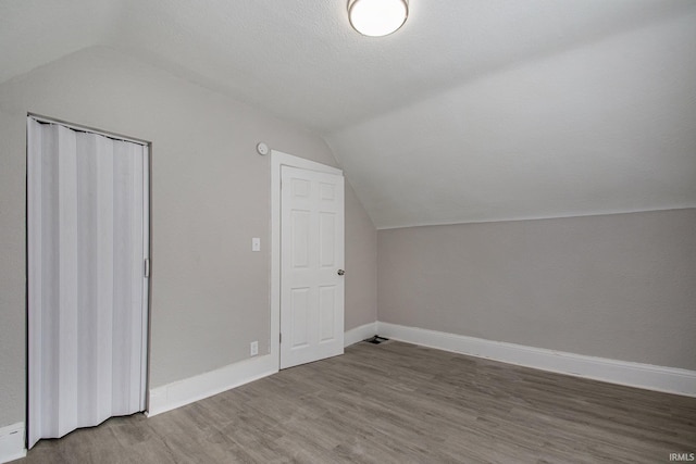 additional living space with wood-type flooring, lofted ceiling, and a textured ceiling