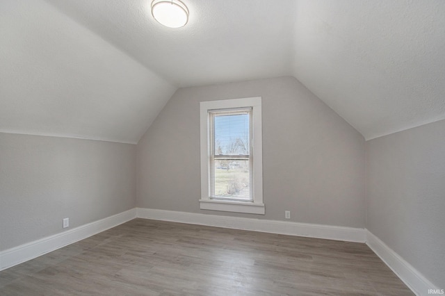 additional living space with lofted ceiling, hardwood / wood-style flooring, and a textured ceiling