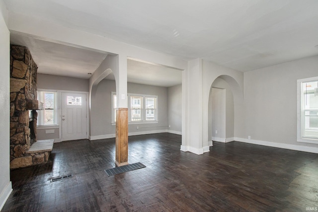 entrance foyer featuring a healthy amount of sunlight, dark hardwood / wood-style flooring, and a stone fireplace