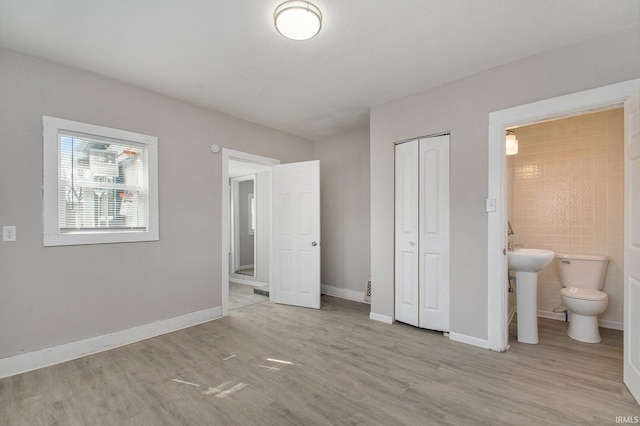 unfurnished bedroom with a closet, light hardwood / wood-style floors, tile walls, and ensuite bathroom