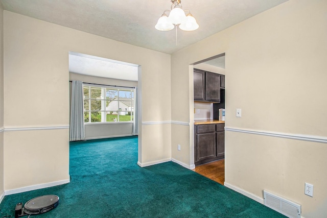 spare room featuring dark carpet and an inviting chandelier