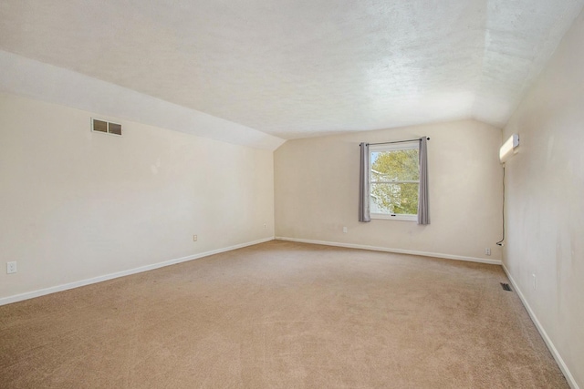 carpeted spare room featuring vaulted ceiling, an AC wall unit, and a textured ceiling