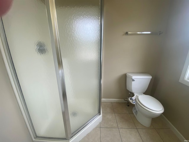 bathroom featuring a shower with door, toilet, and tile flooring